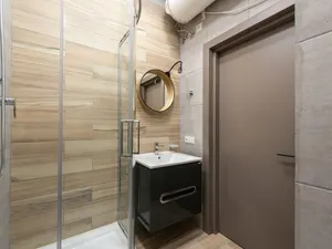 Fertig saniertes kleines Bad mit Duschkabine, Waschtisch, rundem Spiegel und Warmwasserboiler unter der Decke