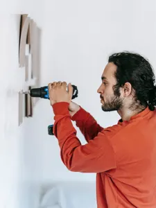 Handwerker bohrt konzentriert im Profil ein Loch in eine weiße Wand, Kartonschablone daneben