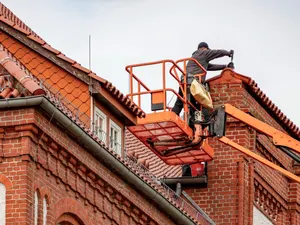 Dachdecker arbeitet vom Hubsteiger aus am Ortgang eines Backsteinhauses