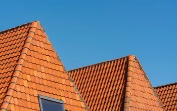 Neu eingedecktes Ziegeldach mit Giebelgauben und Dachfenster vor blauem Himmel