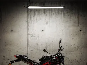 Einzelnes Motorrad seitlich vor roher Betonwand, von einer Leuchtstoffröhre angestrahlt