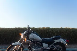 Motorrad im tiefstehenden Abendlicht auf einem leeren Parkplatz, Hecke im Hintergrund