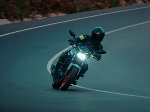 Motorrad in tiefer Schräglage auf einer dunklen Landstraßenkurve, Scheinwerfer eingeschaltet