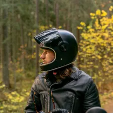 Fahrlehrer im Profil mit Integralhelm und Lederjacke, zieht am Waldrand die Handschuhe an
