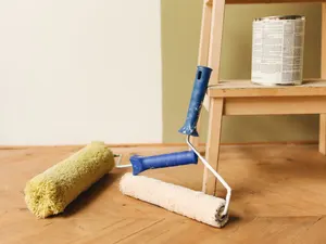 Zwei Farbwalzen und eine Farbdose vor einer salbeigrünen Wand auf Dielenboden