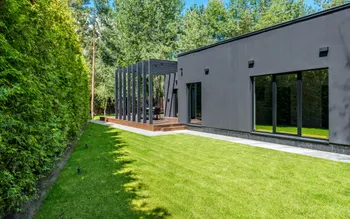 Fertig angelegter Garten mit Rasenfläche, Pergola über Holzterrasse und hoher Hecke