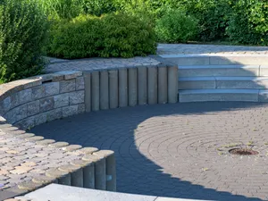 Terrasse mit Granitstufen, Palisaden und Pflasterbelag, dahinter geschnittene Gehölze und Hecke