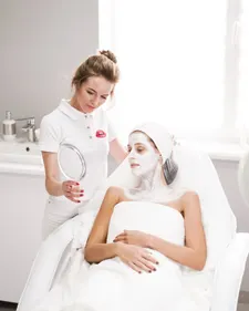 Kosmetikerin trägt einer Kundin eine Maske auf, heller Raum