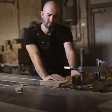 Tischler mit Arbeitsschürze arbeitet konzentriert an der Maschine in der Werkstatt