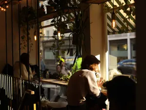 Gäste am Fensterplatz im Gegenlicht des Nachmittags, Hängepflanzen und Blick auf die Straße.