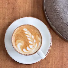 Flat White von oben: Milchschaum-Rosette in weißer Tasse auf warmem Holztisch.