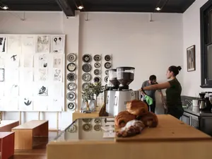 Heller Cafétresen am Vormittag: Siebträgermaschine, Mühlen und frische Croissants, dahinter arbeitet das Team.