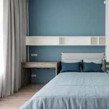 Reduziertes Schlafzimmer mit Leinenbettwäsche in Blautönen, Wandregal und Vorhang am Fenster