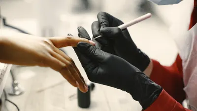 Nageldesignerin in schwarzen Handschuhen arbeitet konzentriert an einer Hand