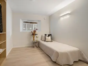 Schmales Einzelzimmer mit Einzelbett an der Wand, offenem Regal und kleinem Fenster