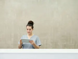Empfangstresen der Praxis, dahinter eine Mitarbeiterin mit Tablet vor heller Wandfläche