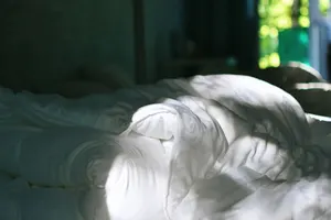 Abgezogenes Bett mit weißer Decke, Morgenlicht fällt durch die offene Tür