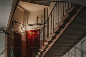 Treppenhaus eines Altbaus mit Steinstufen, schmiedeeisernem Geländer und roter Wohnungstür