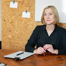 Hausverwalterin am Besprechungstisch mit Notizblock und Stift, dahinter Pinnwand und Whiteboard