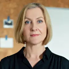 Porträt einer Steuerberaterin mit blondem Bob, sachlicher Blick, neutrales Büro mit Pinnwand im Hintergrund