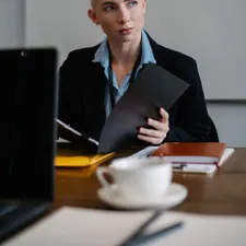 Junge Steuerfachangestellte im dunklen Blazer mit Mappe, im Hintergrund ein Whiteboard im Besprechungsraum