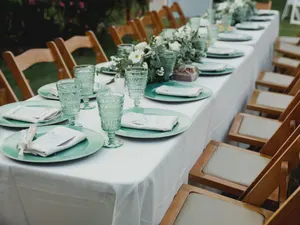 Lange, leer gedeckte Tafel im Garten mit grünem Geschirr und Blumenschmuck