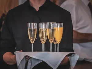 Servicekraft trägt ein Tablett mit Sekt und Orangensaft durch den Empfang