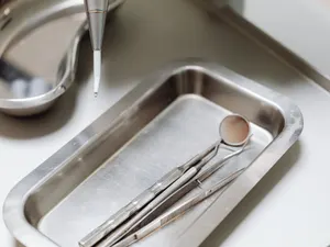 Mundspiegel, Sonde und Pinzette auf einer Edelstahlablage neben einer Nierenschale