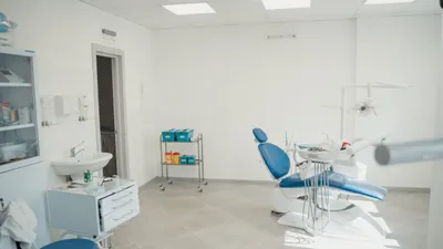 Heller, ruhiger Behandlungsraum mit weißen Wänden, blauem Stuhl und Tageslicht auf dem Boden